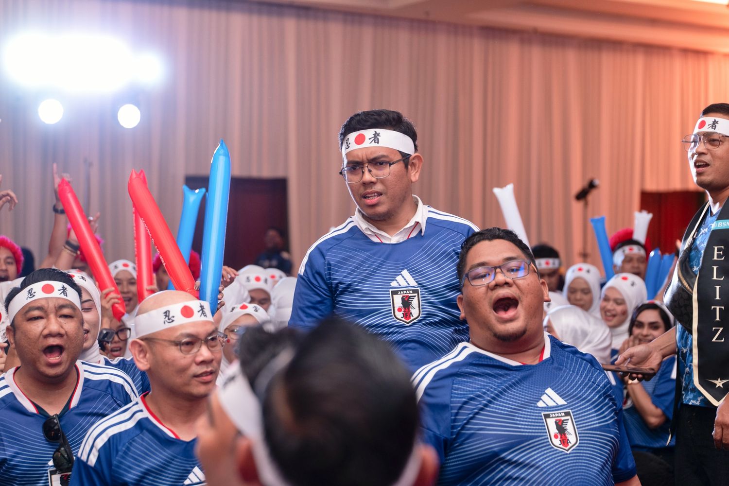 Enthusiastic crowd wearing Japan football jerseys and headbands cheering at a corporate event.