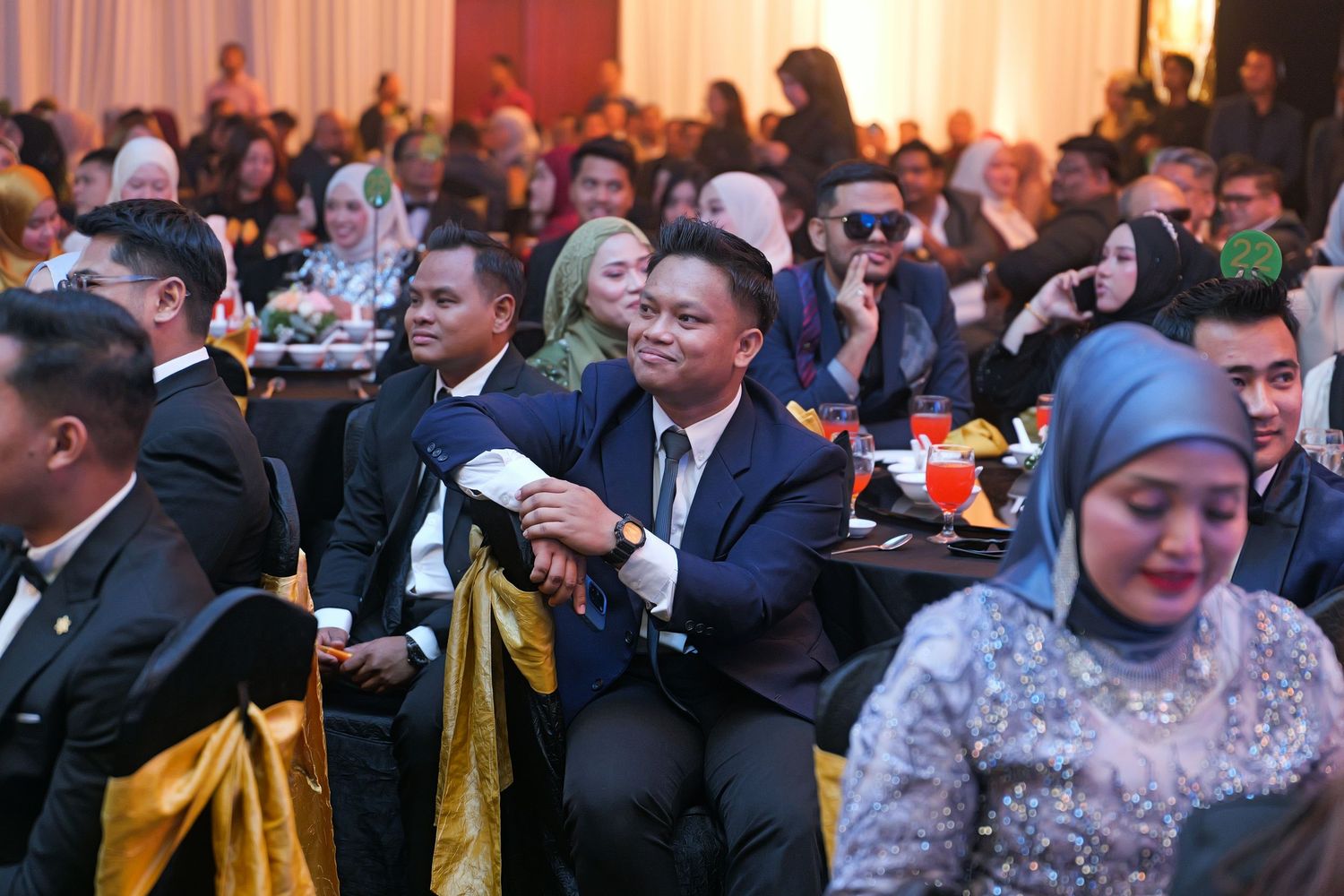 Guests in formal attire seated at tables during a Malaysian gala dinner event in a grand ballroom.