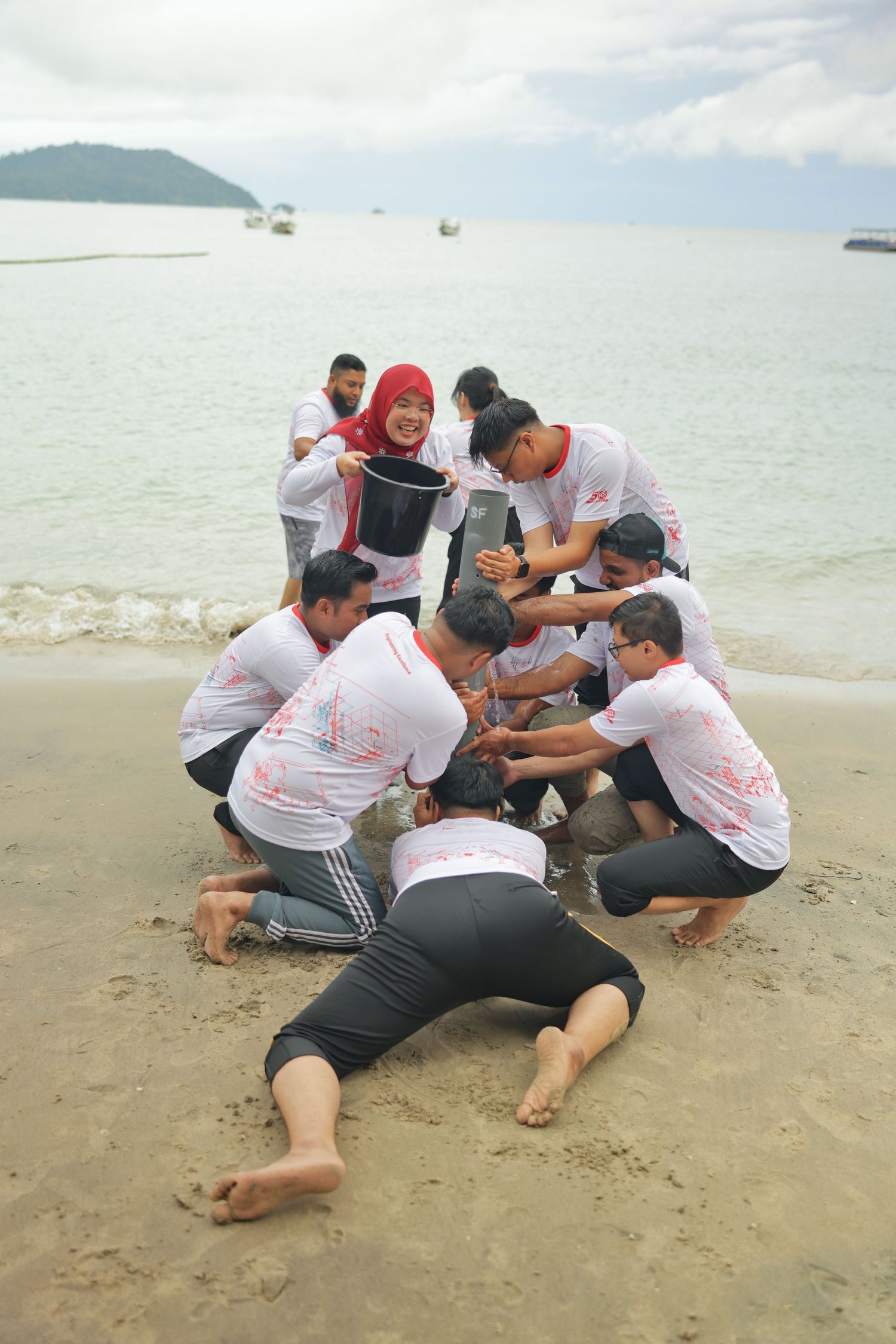 Team building activity on beach with group of people in matching white shirts working together on sandy shore.