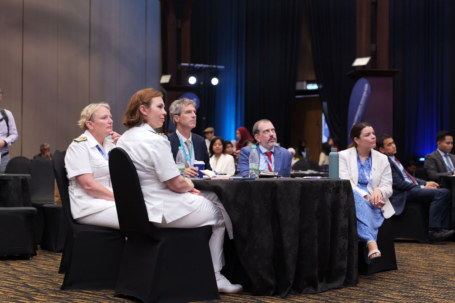 Panel discussion setup with speakers seated at a long table during a professional conference.