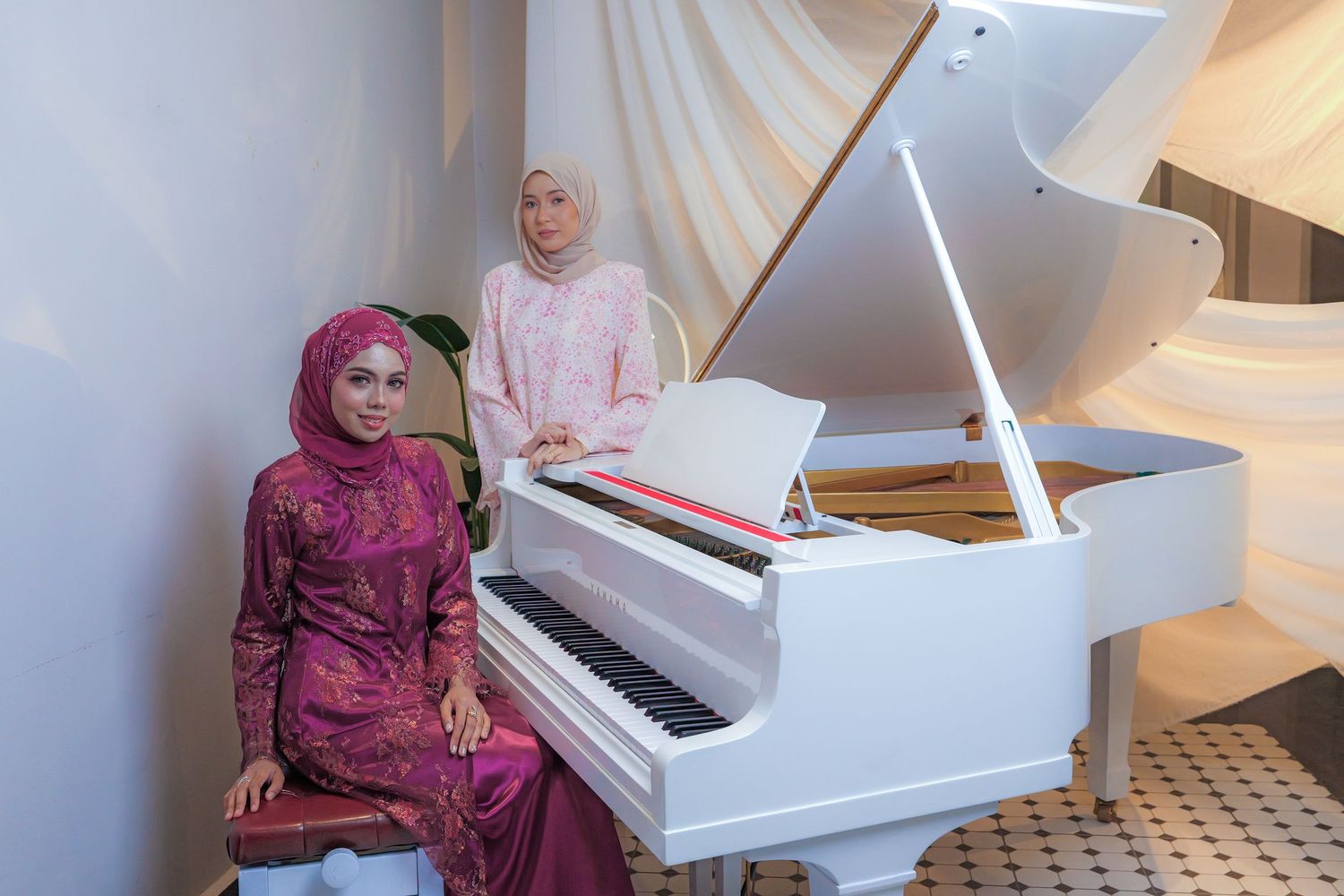 A white grand piano sits in an elegant room with draped white fabric backdrop and patterned tile flooring.