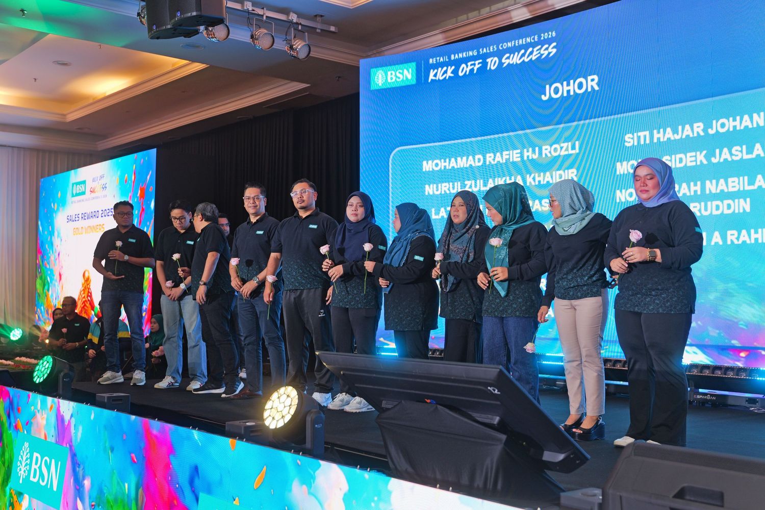 Corporate team members standing on stage at a BSN Johor regional event presentation.