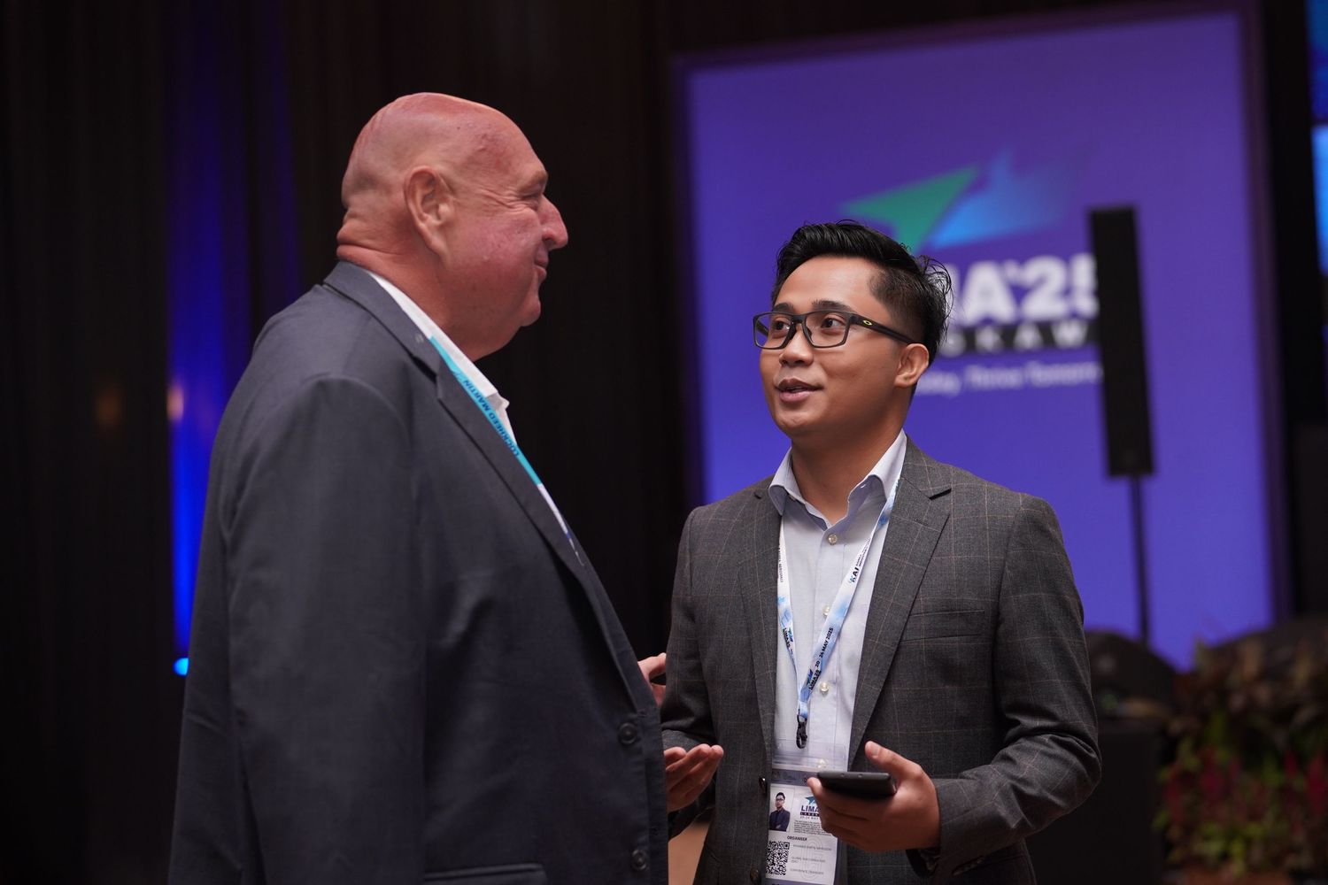 Two professionals engaged in conversation at a business conference with purple lighting and branding.