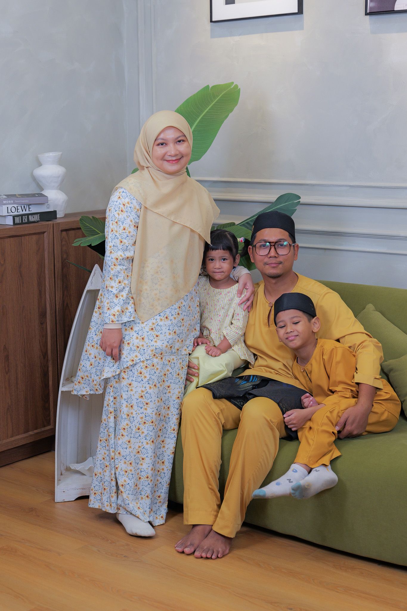 Family members wearing yellow and floral outfits sit together on a green couch in a living room setting.