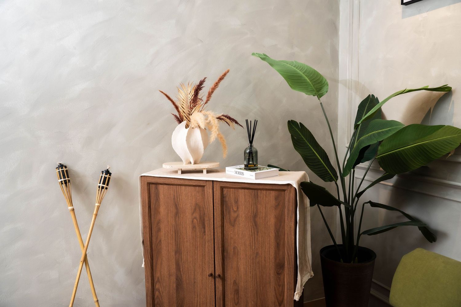 Modern living room with wooden furniture, crossed decorative skis, and potted plants against a gray concrete wall.