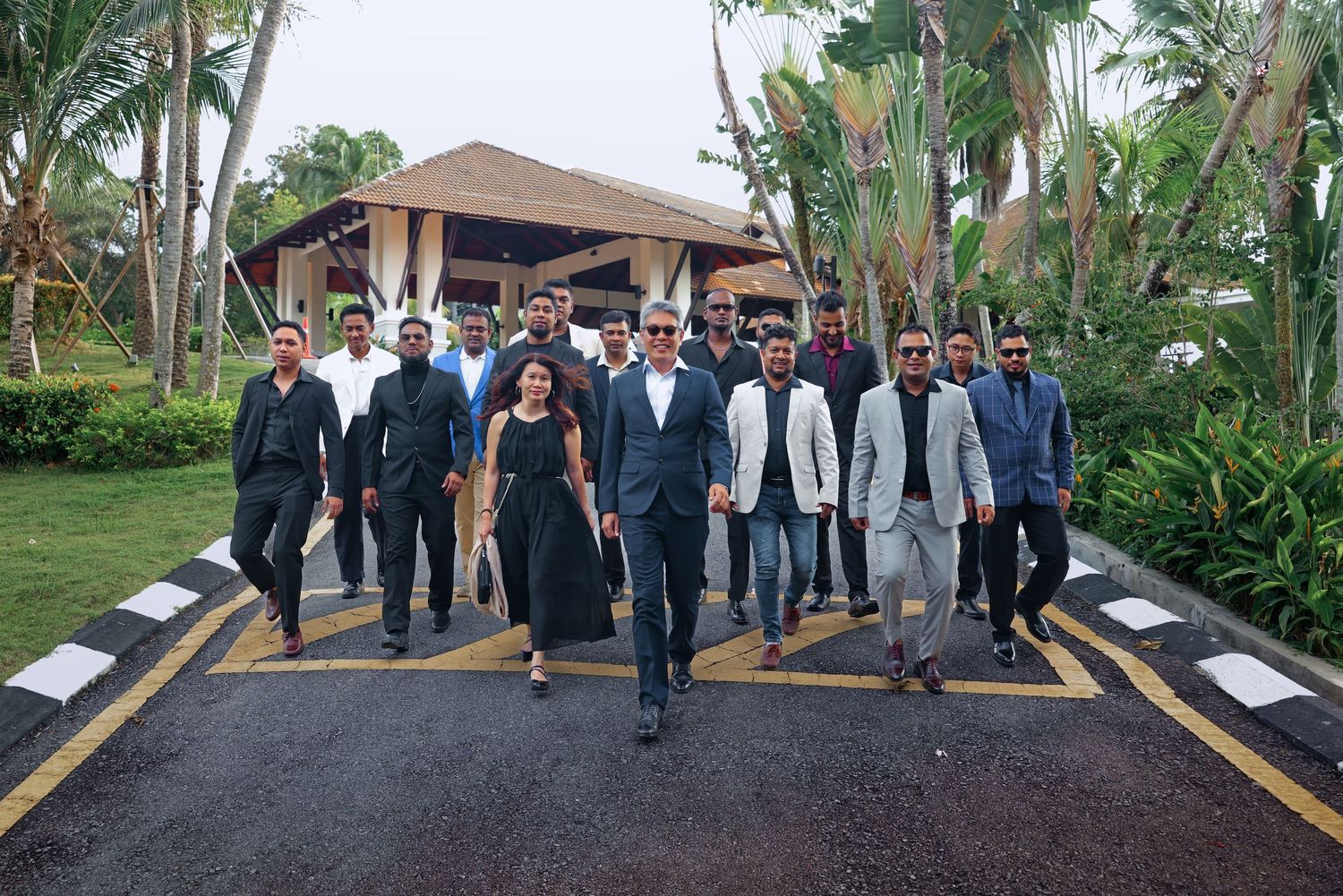 Group of well-dressed professionals walking confidently down a tropical resort pathway in formal attire.