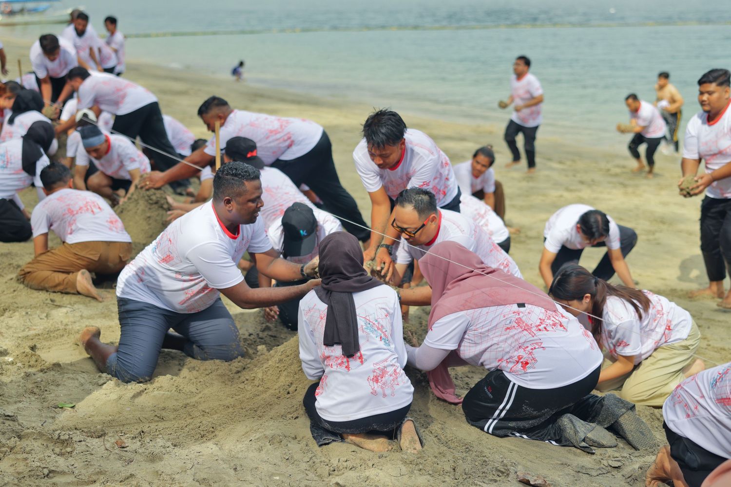 Large group of people in matching white shirts engaged in a competitive beach sand digging team building exercise.