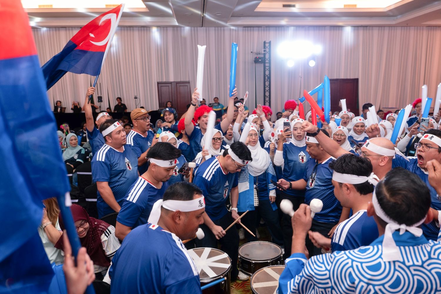 Energetic crowd in blue uniforms plays drums and waves flags at an exciting indoor event.