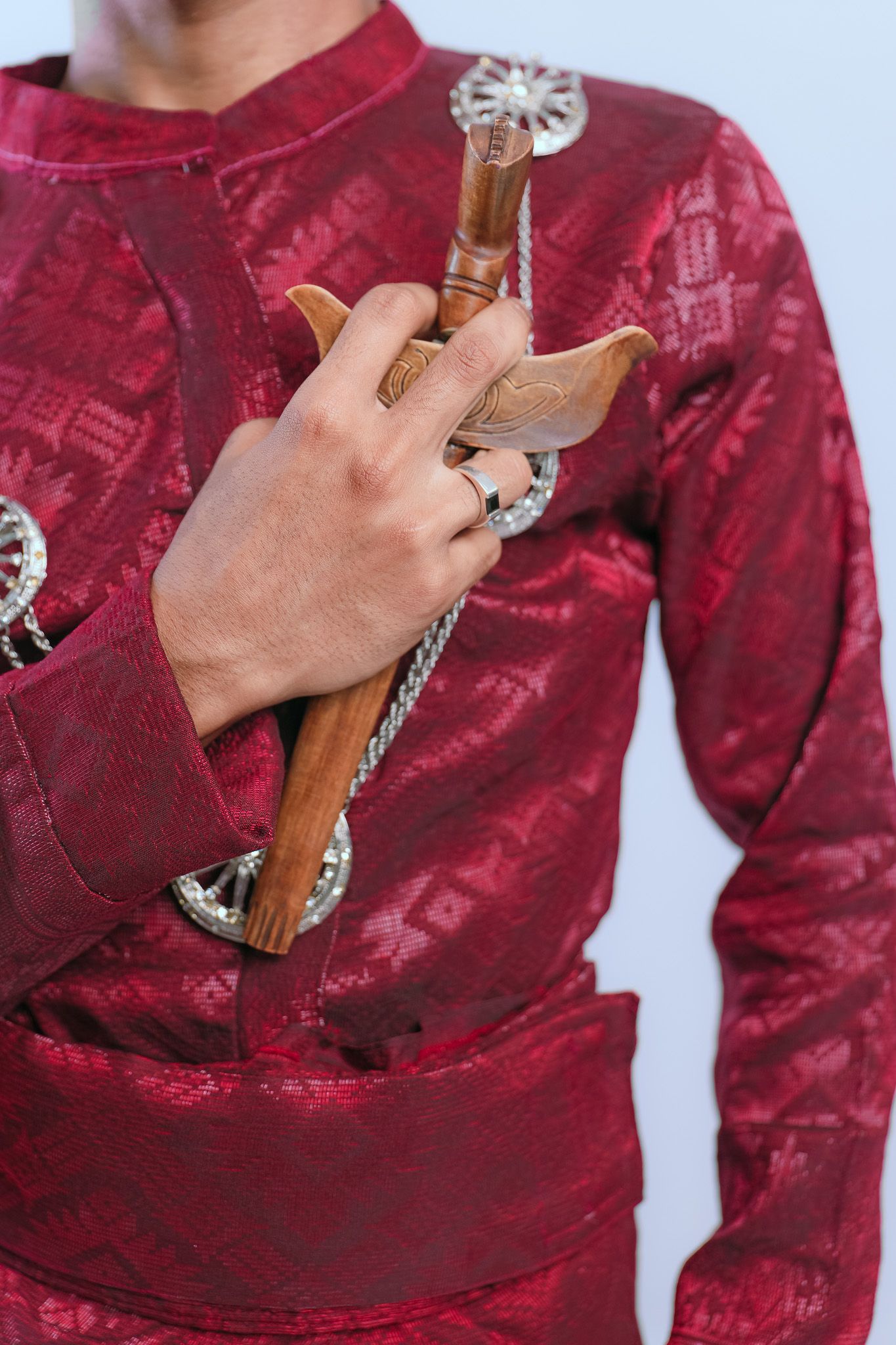 Close-up of hand holding traditional Malay wooden wedding dagger against red ceremonial dress.