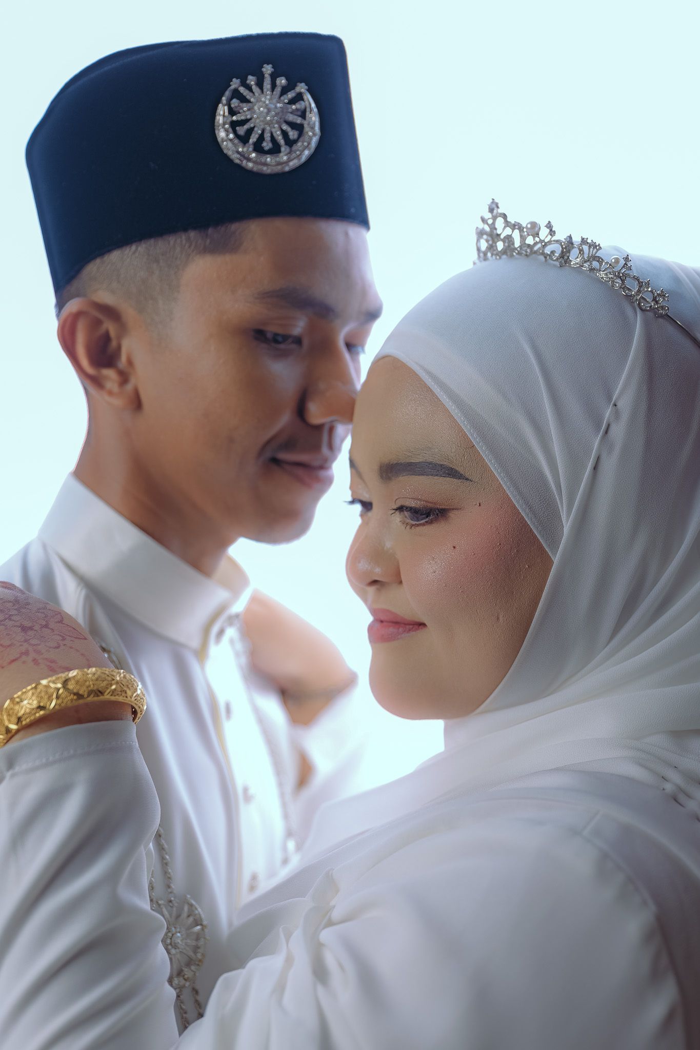 Muslim bride and groom in traditional white attire share a tender wedding portrait moment.