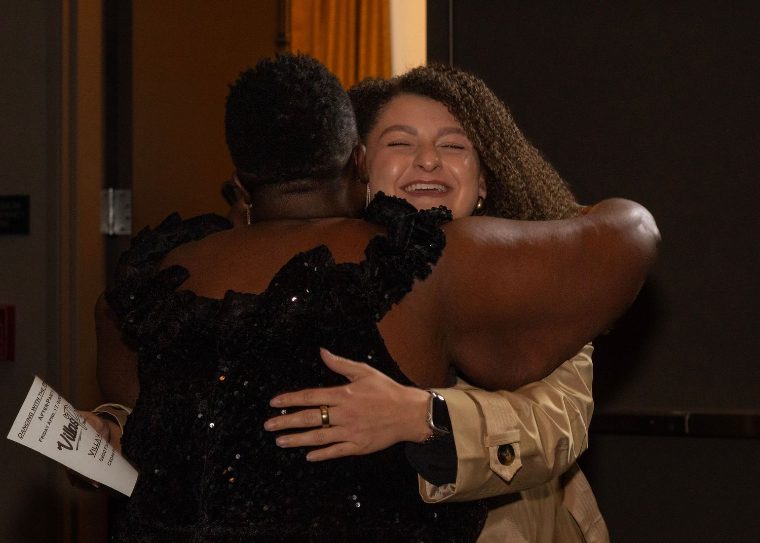 Two women sharing a warm hug at a formal event, one wearing a black sequined dress.