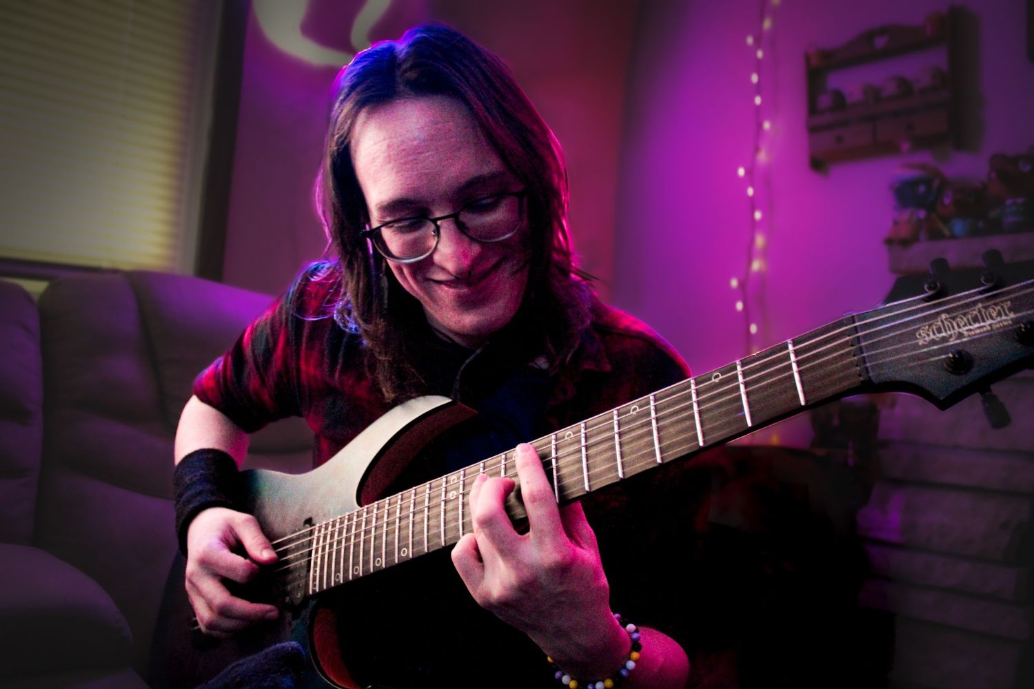 A musician plays electric guitar in a room with purple ambient lighting.