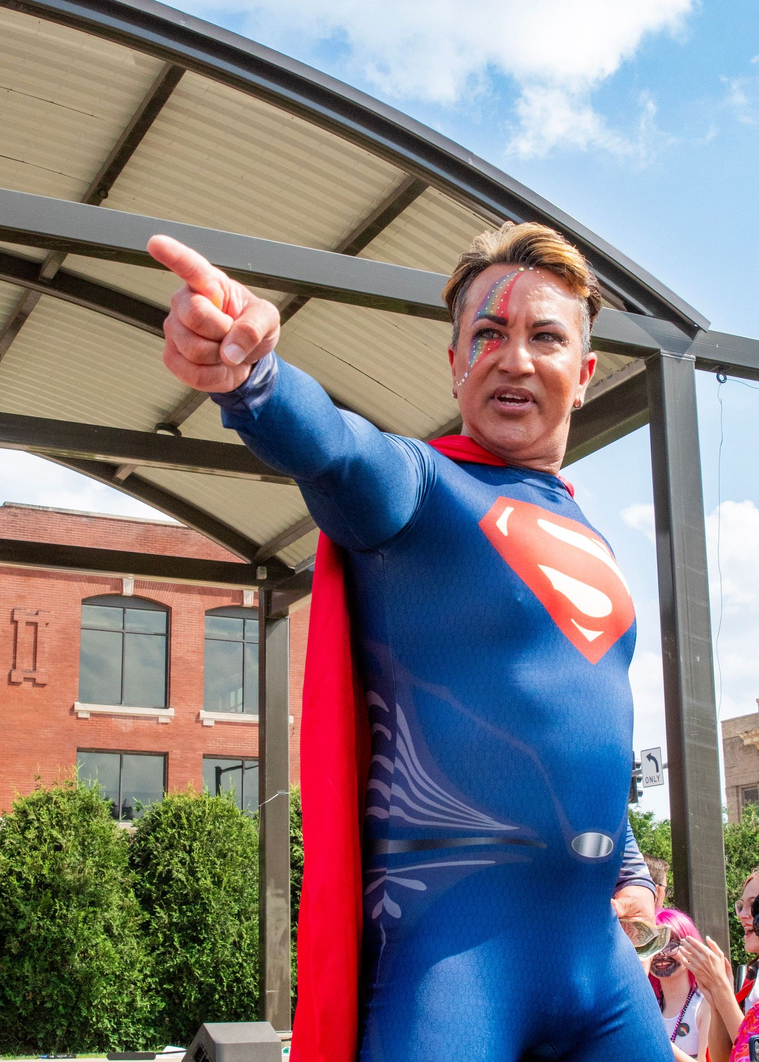 A person in a Superman costume points and gestures while standing under a covered outdoor area.