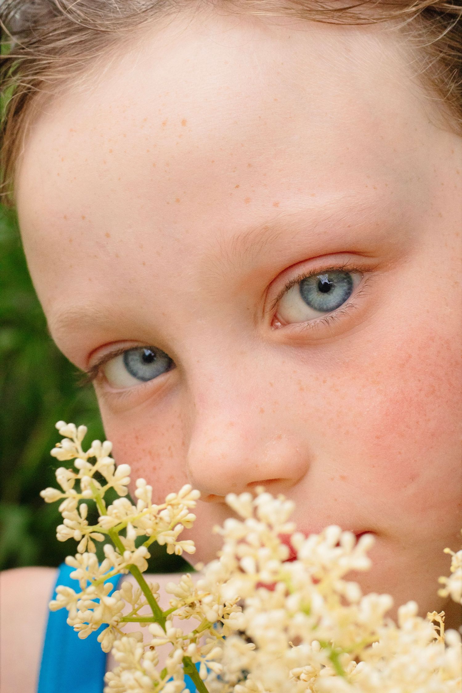 Close-up portrait of a blue-eyed child with freckles smelling white wildflowers outdoors.