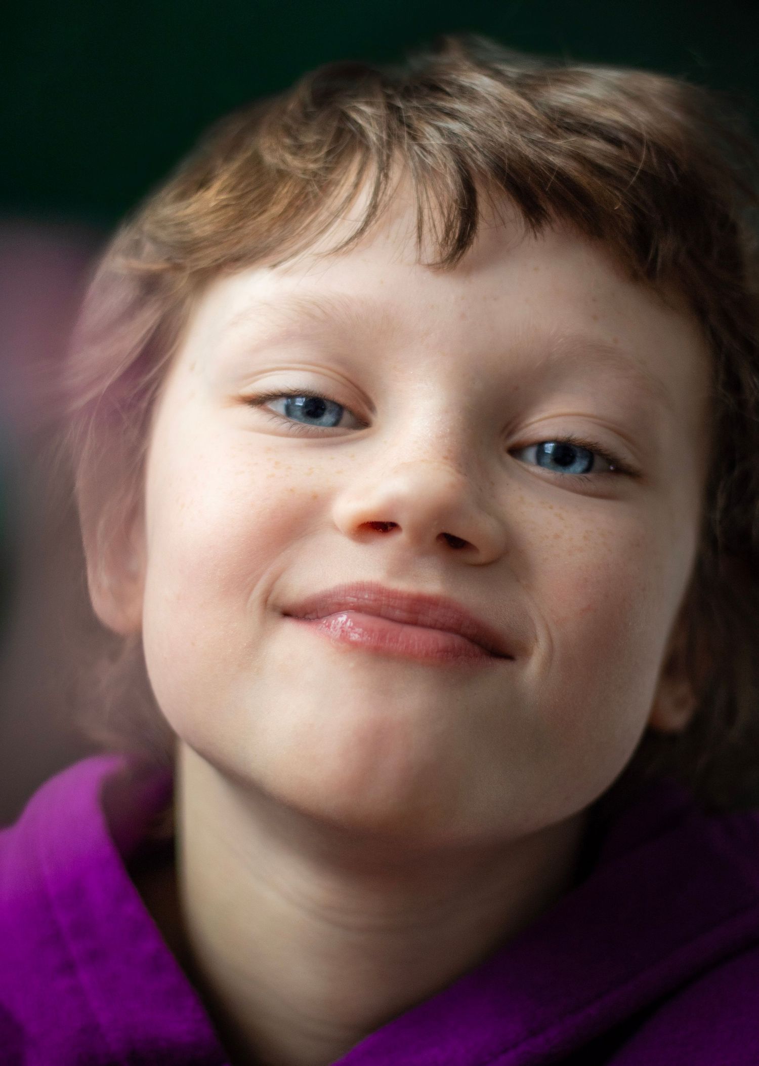 A cheerful young child with blue eyes and freckles smiling warmly, wearing a purple hoodie.