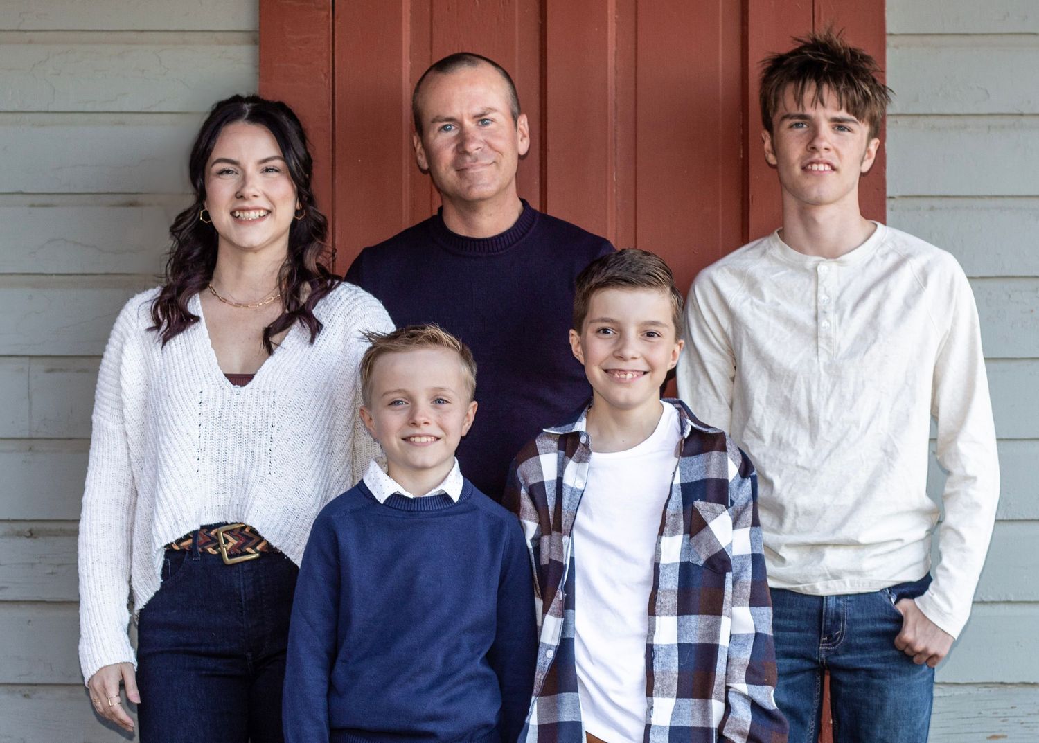A family group poses together on a porch wearing coordinated blue and white casual outfits for a portrait.