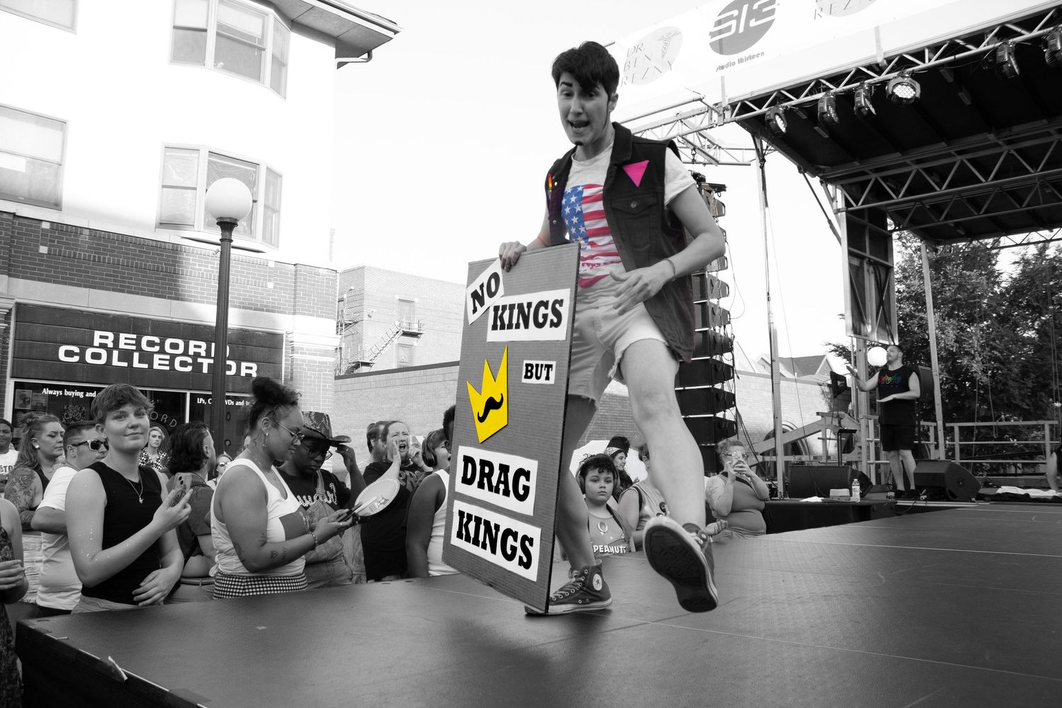 Black and white photo of performer dancing on outdoor stage with signs.