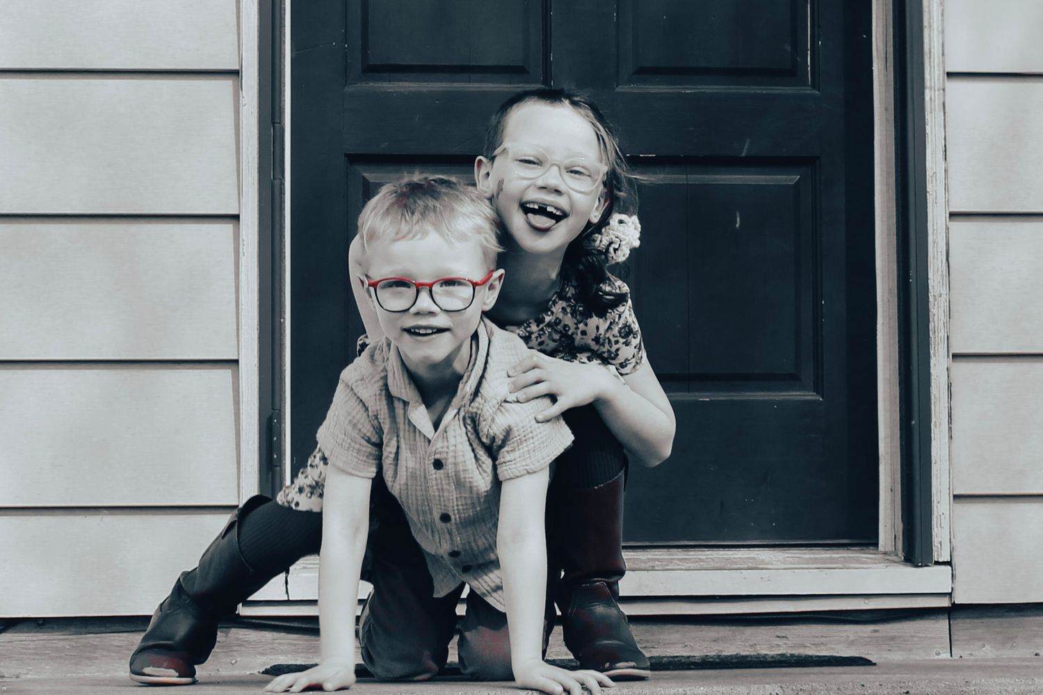 Two playful figures pose together on a front porch in a black and white composition.