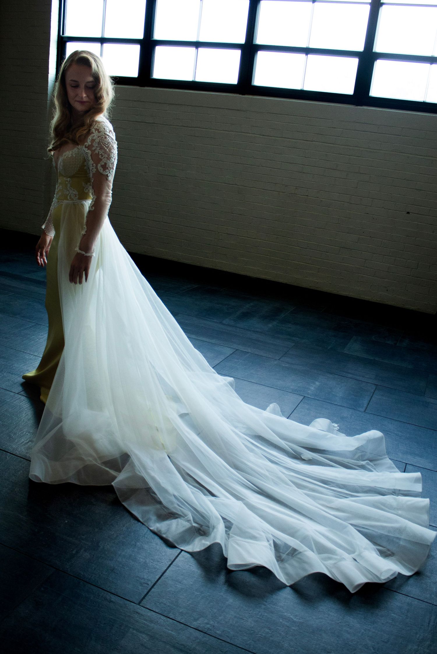 A flowing white wedding dress with a dramatic train photographed in an industrial space with natural window light.