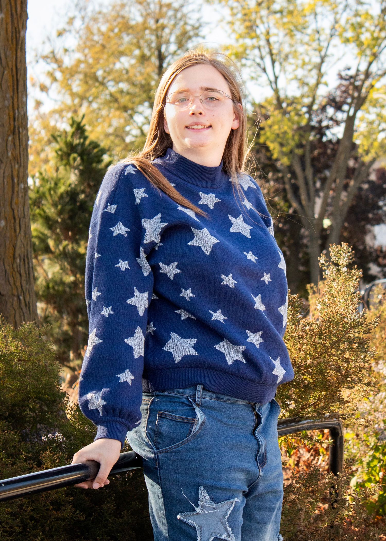 A blue sweater with silver star pattern is paired with jeans in an autumn outdoor setting.