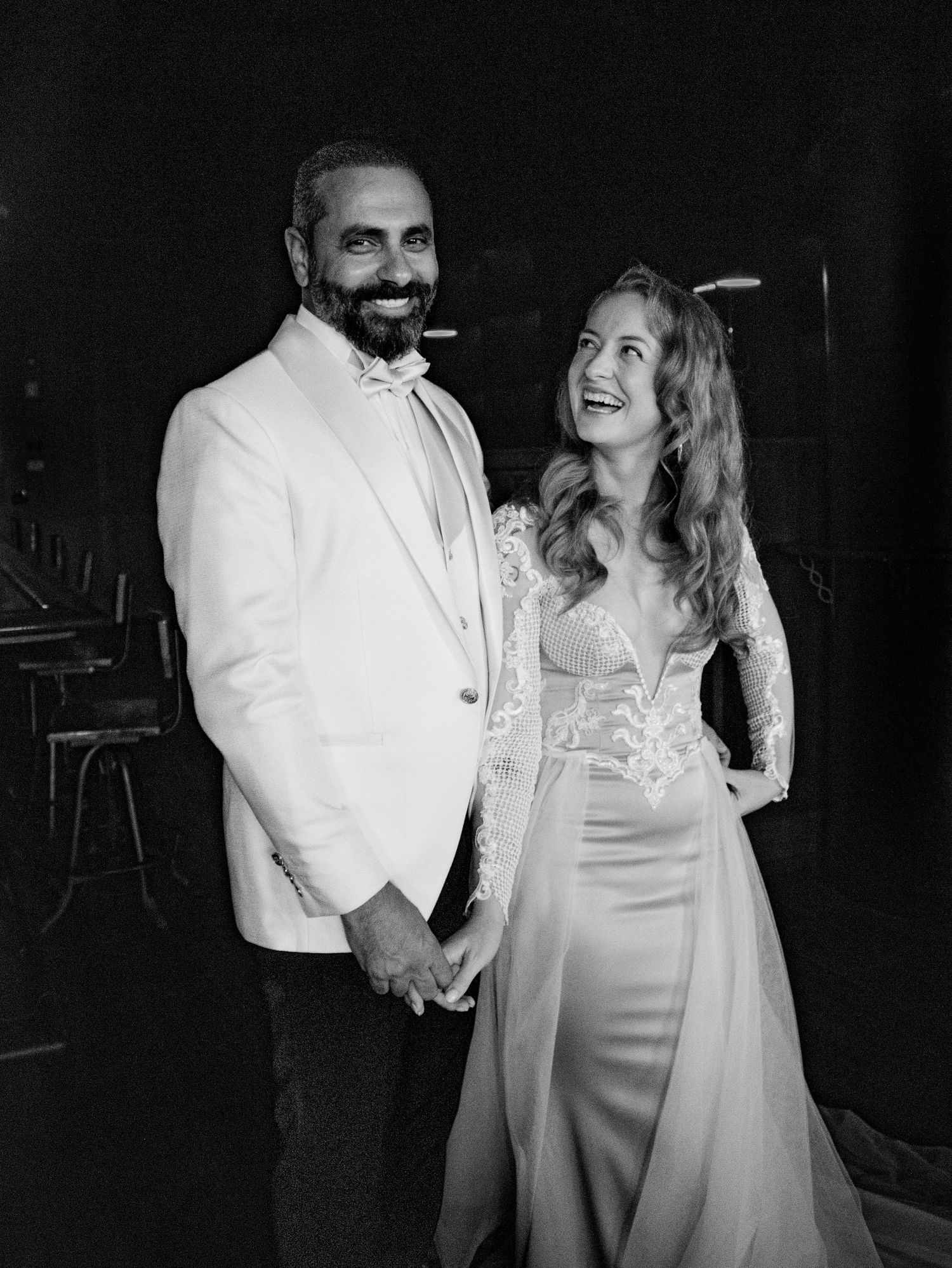 A couple shares joyful candid moments in formal attire during what appears to be a wedding celebration.