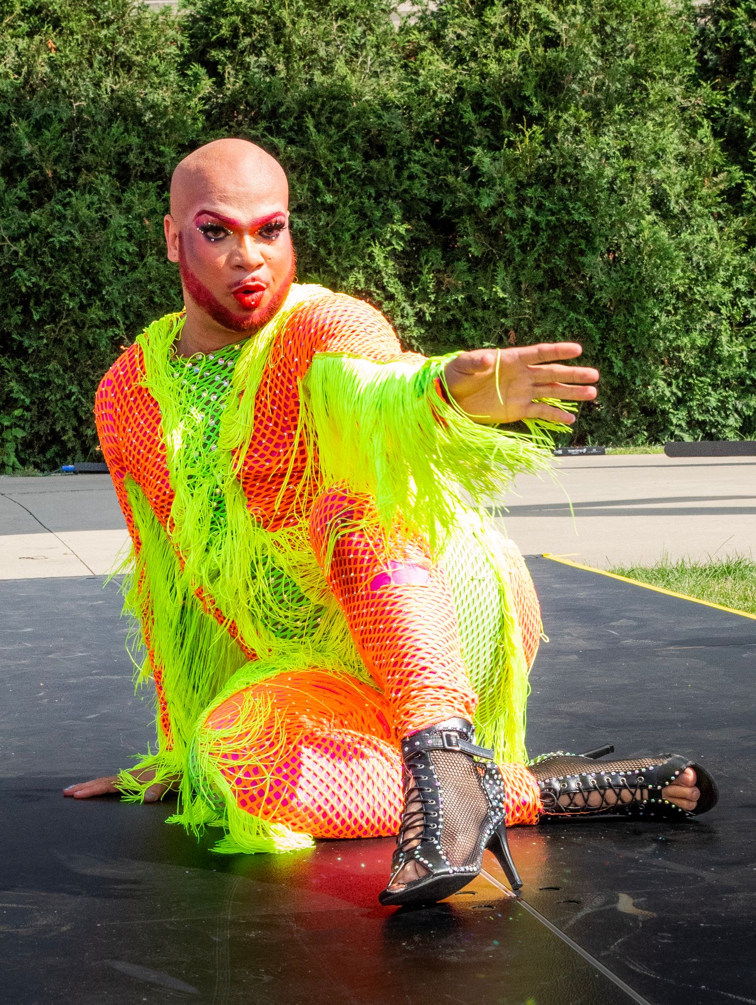 A performer in a neon yellow and orange costume executes a dramatic breakdance move on a black surface.