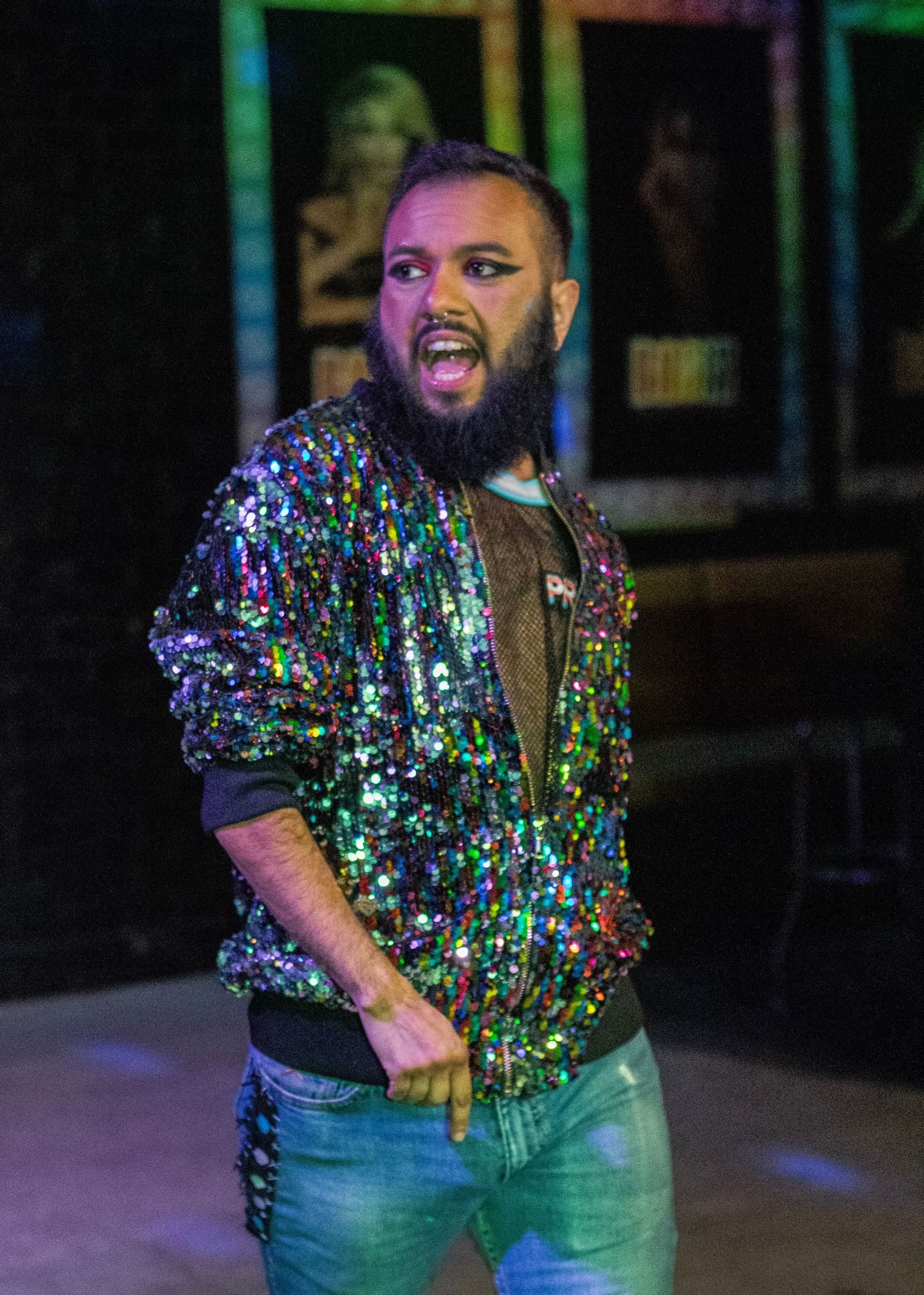 Performer in sparkly sequined shirt dancing under colorful stage lighting.