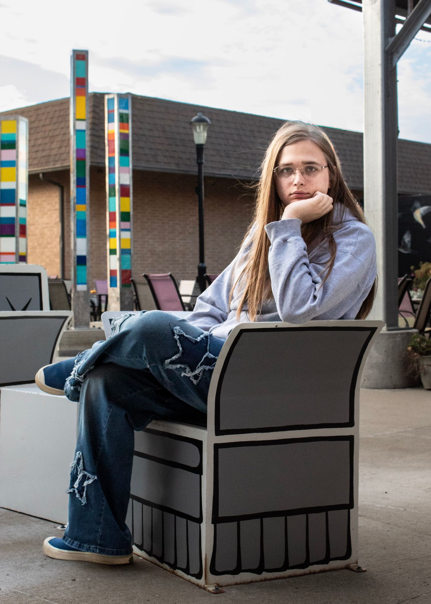 Someone relaxes in a modern black bench seating area with colorful striped pillars in the background.