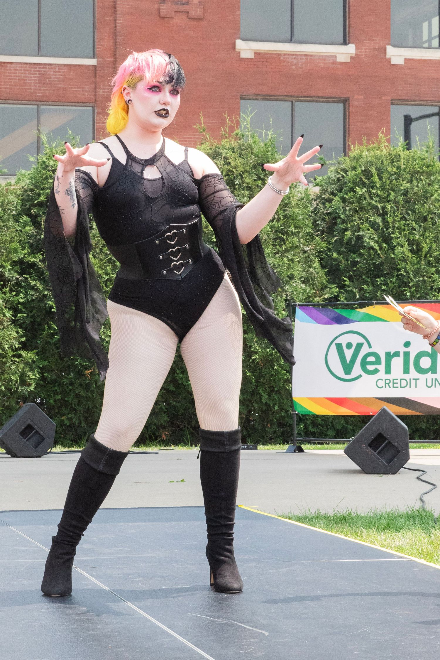 A dancer in black attire performs expressive movements on an outdoor stage with brick buildings in the background.