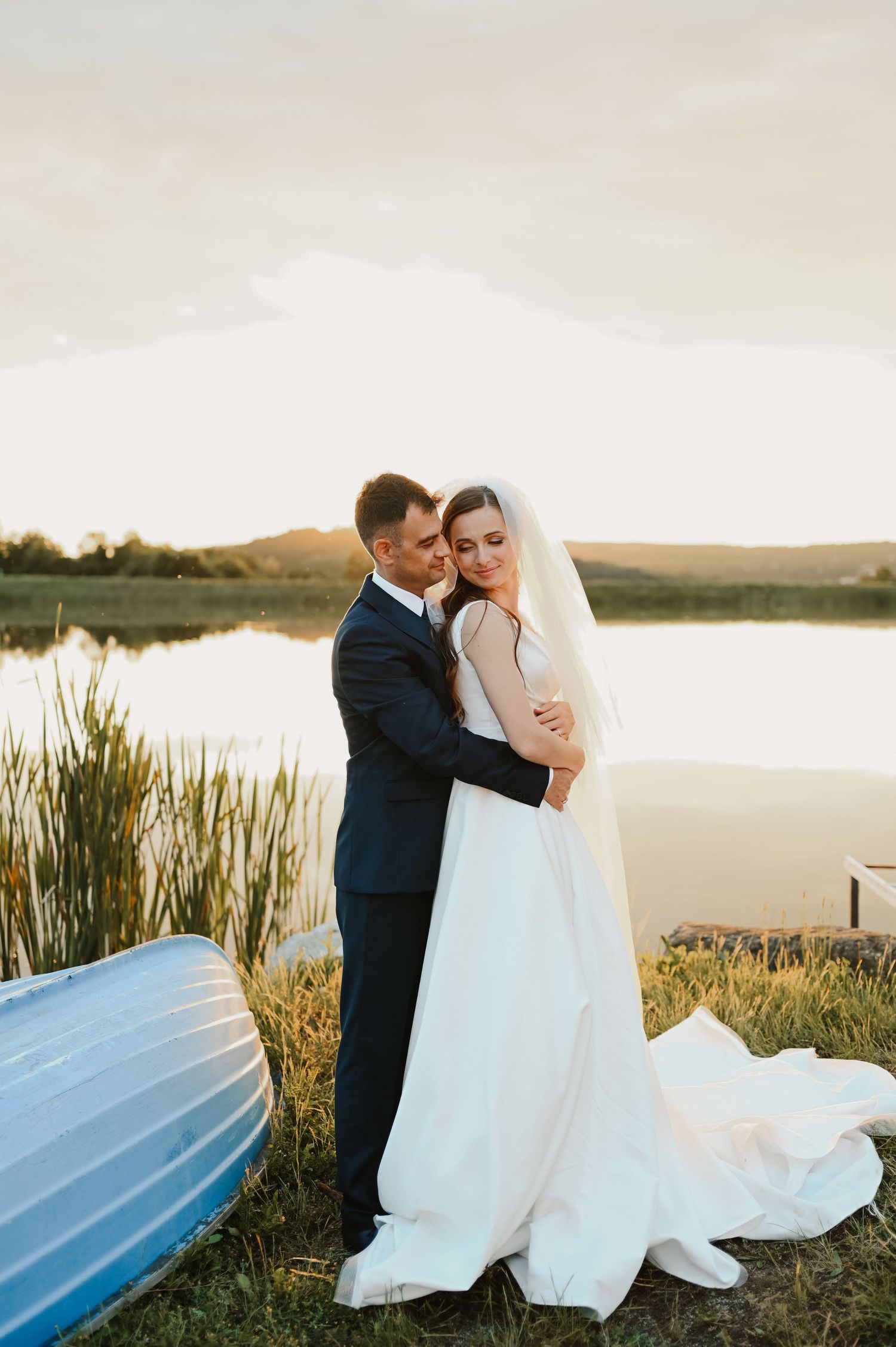 Romantic sunset wedding photo by a lake with a blue canoe in the background.