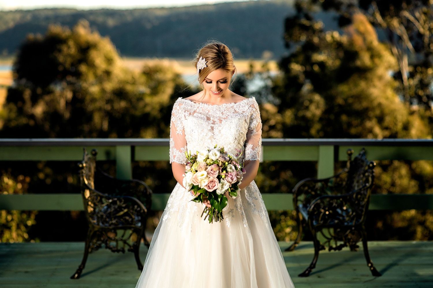 Elegant bride poses outdoors in a white wedding dress surrounded by natural scenery.