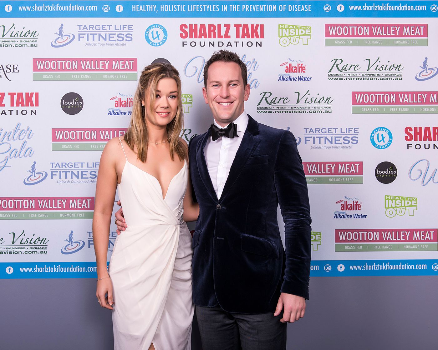 Corporate event photography Sydney. Brand ambassadors posing on red carpet at formal event with sponsor backdrop.
