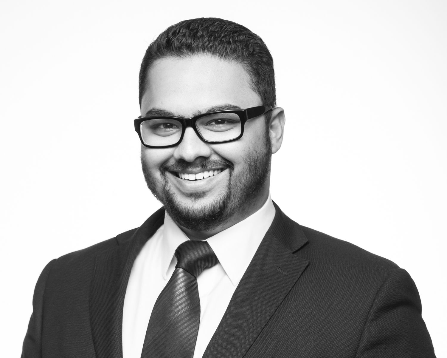 Professional headshot photo against a white background showing someone in formal business attire and glasses.
