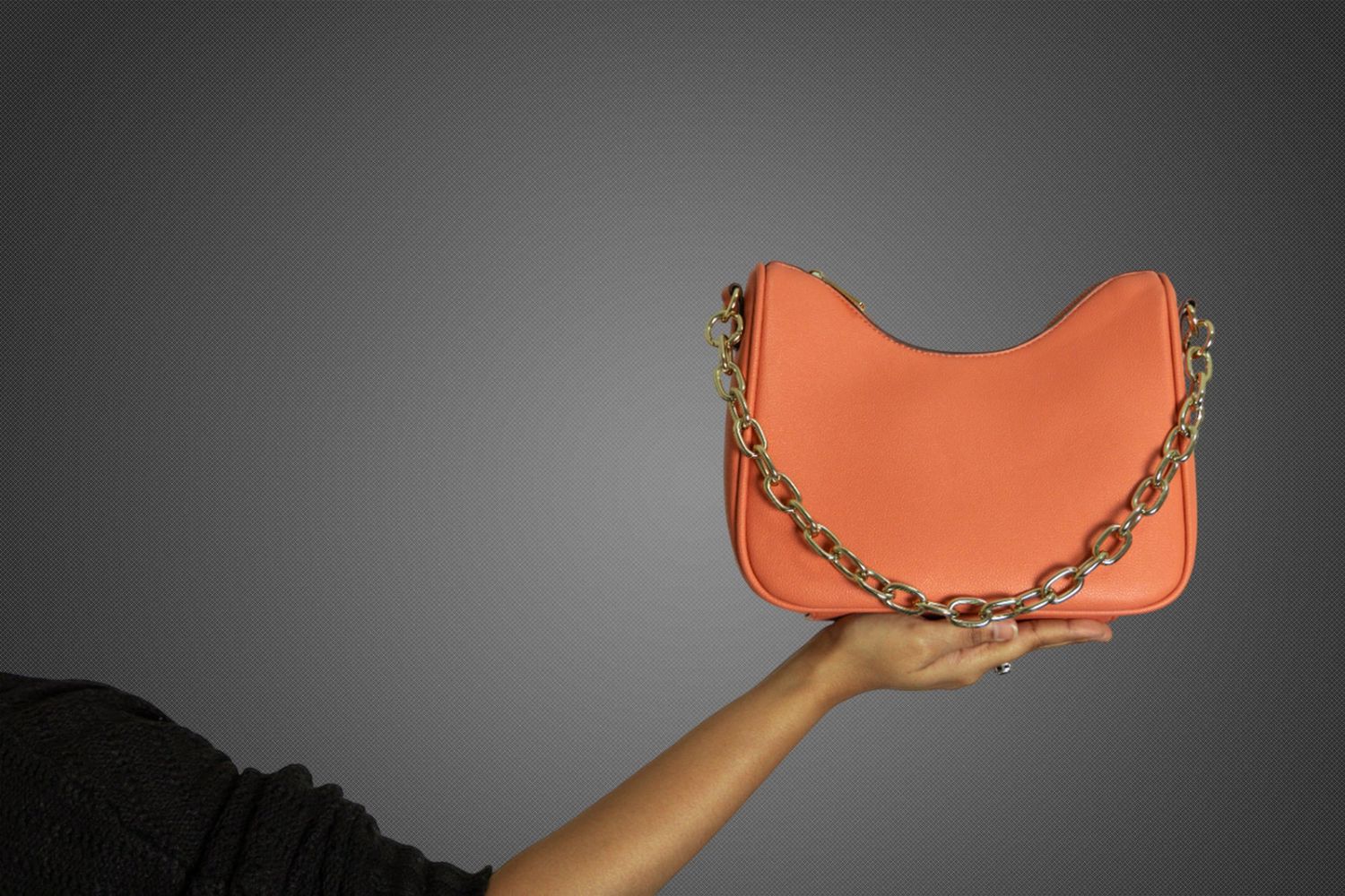 Product photography Sydney. Hand holding an orange designer purse with chain detail while posing against a dark background.