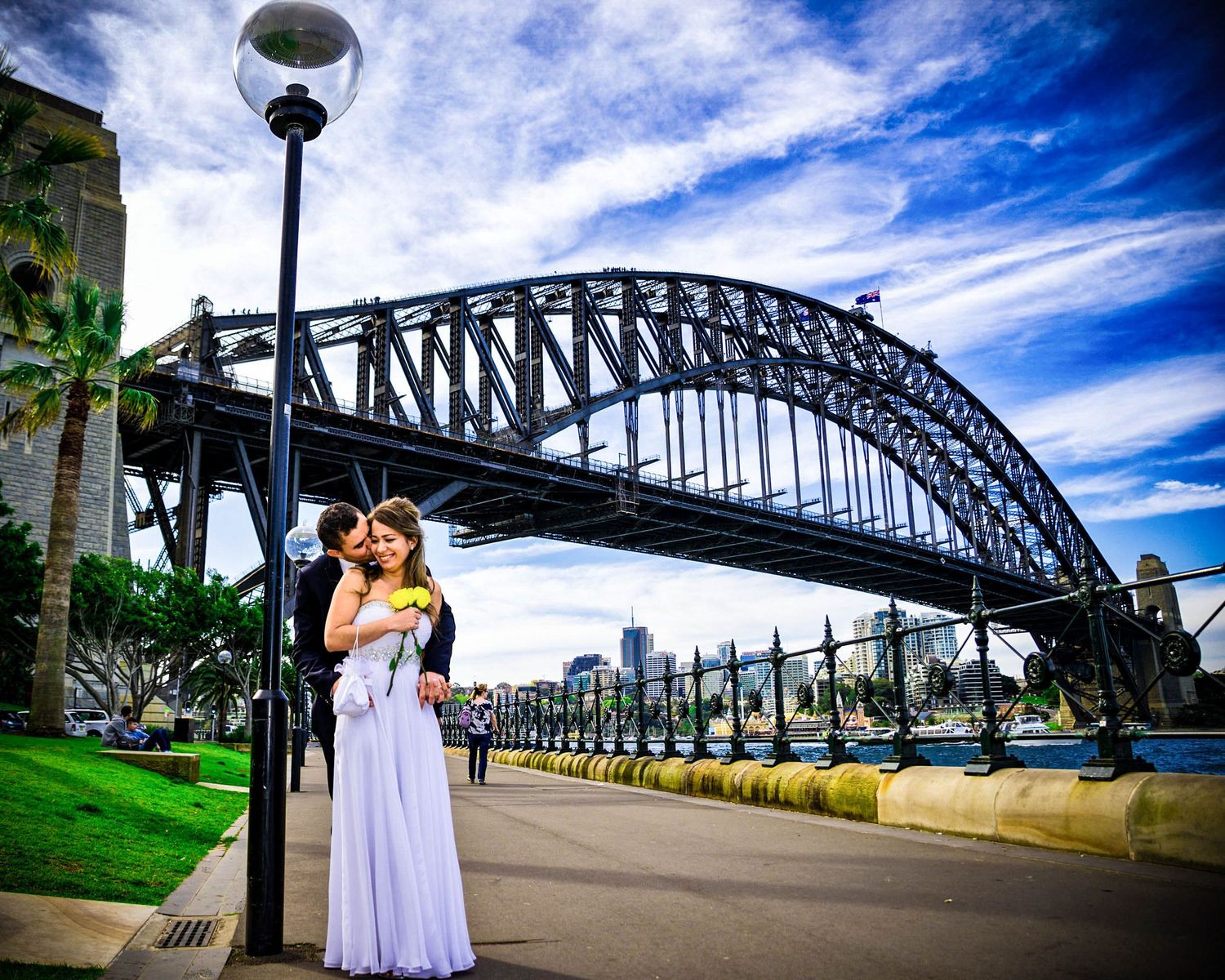 A wedding couple is hugging each other in front of the Sydney Harbour Bridge.