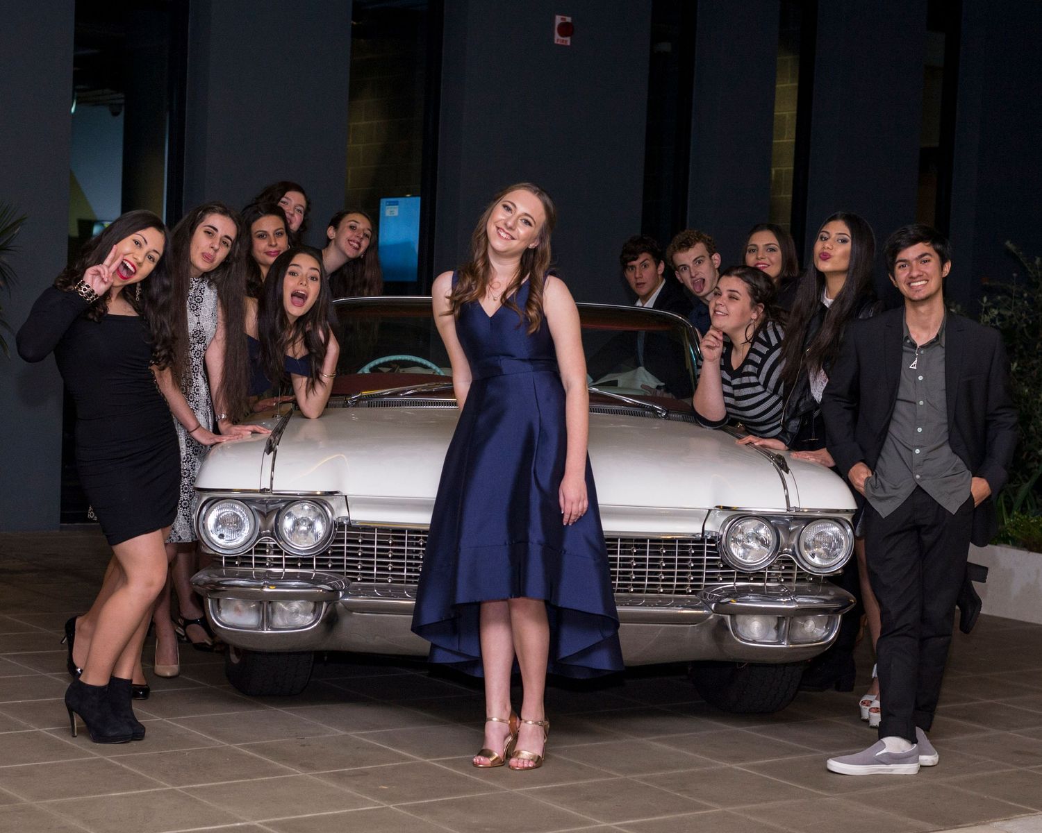 Group photo with vintage Cadillac car and people in formal attire.