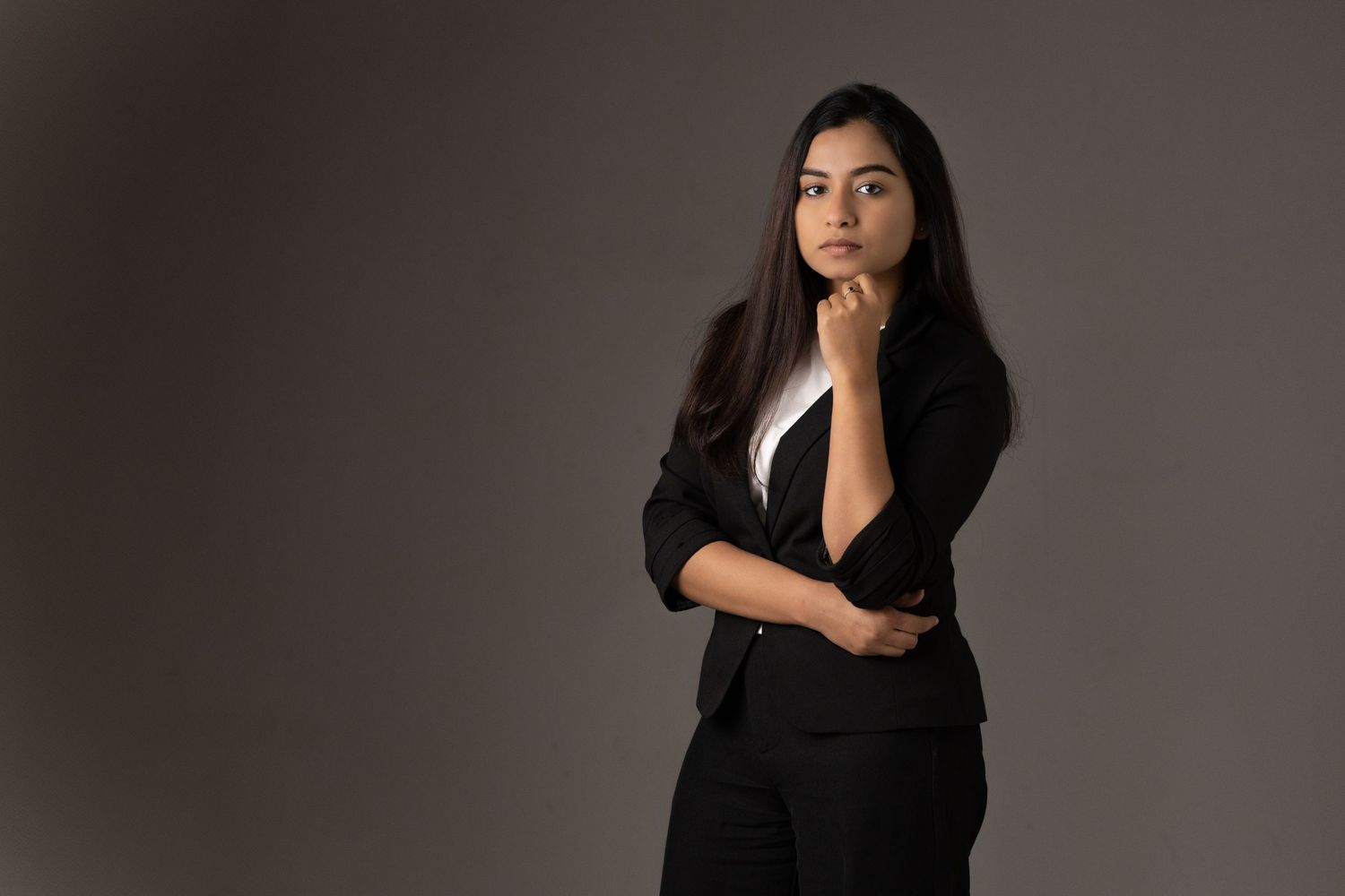 A model in a black v-neck top poses pensively against a dark grey backdrop in a professional portrait headshot series.