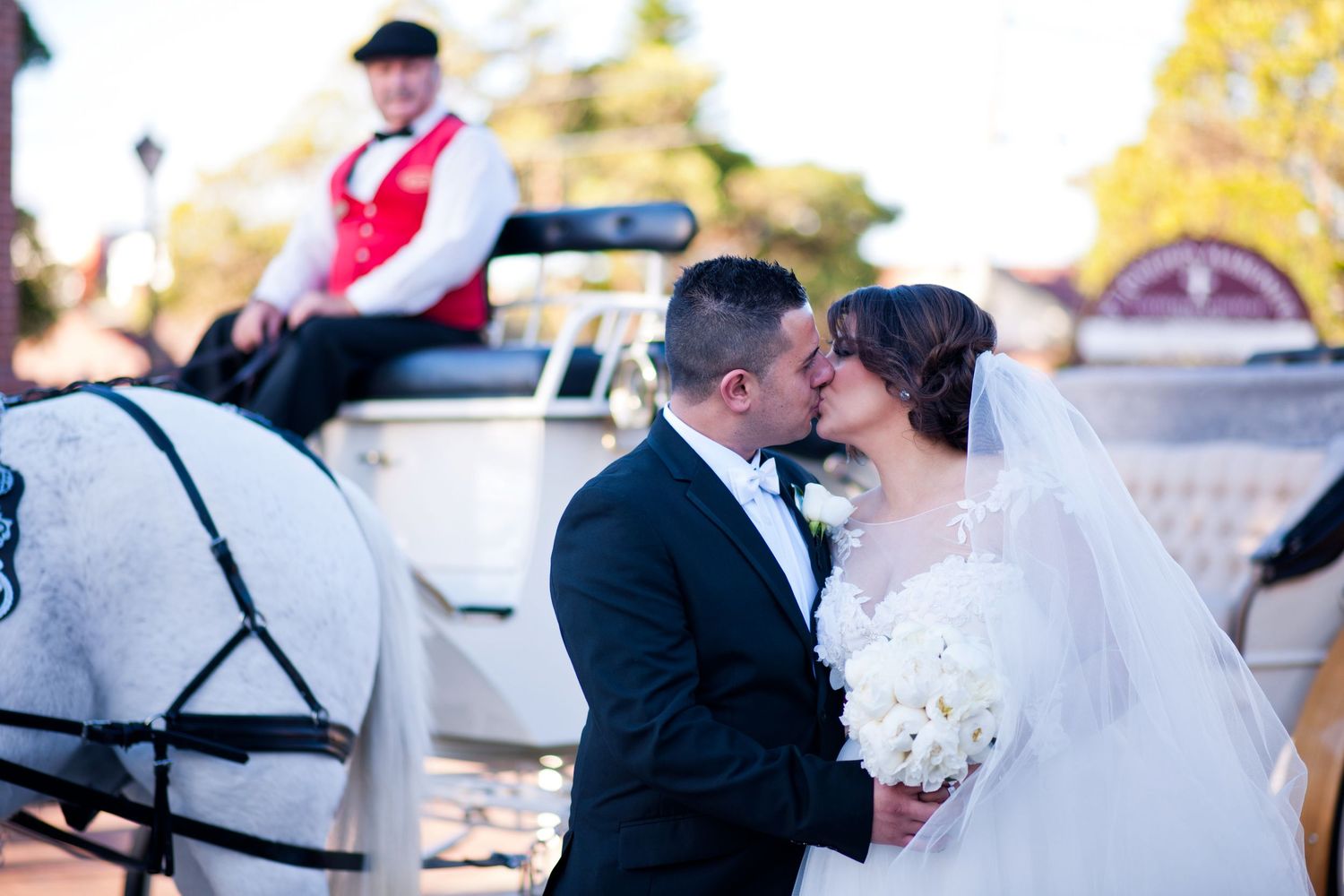 A romantic moment by a white horse-drawn carriage at sunset during an elegant wedding celebration, where the couple is kissing.