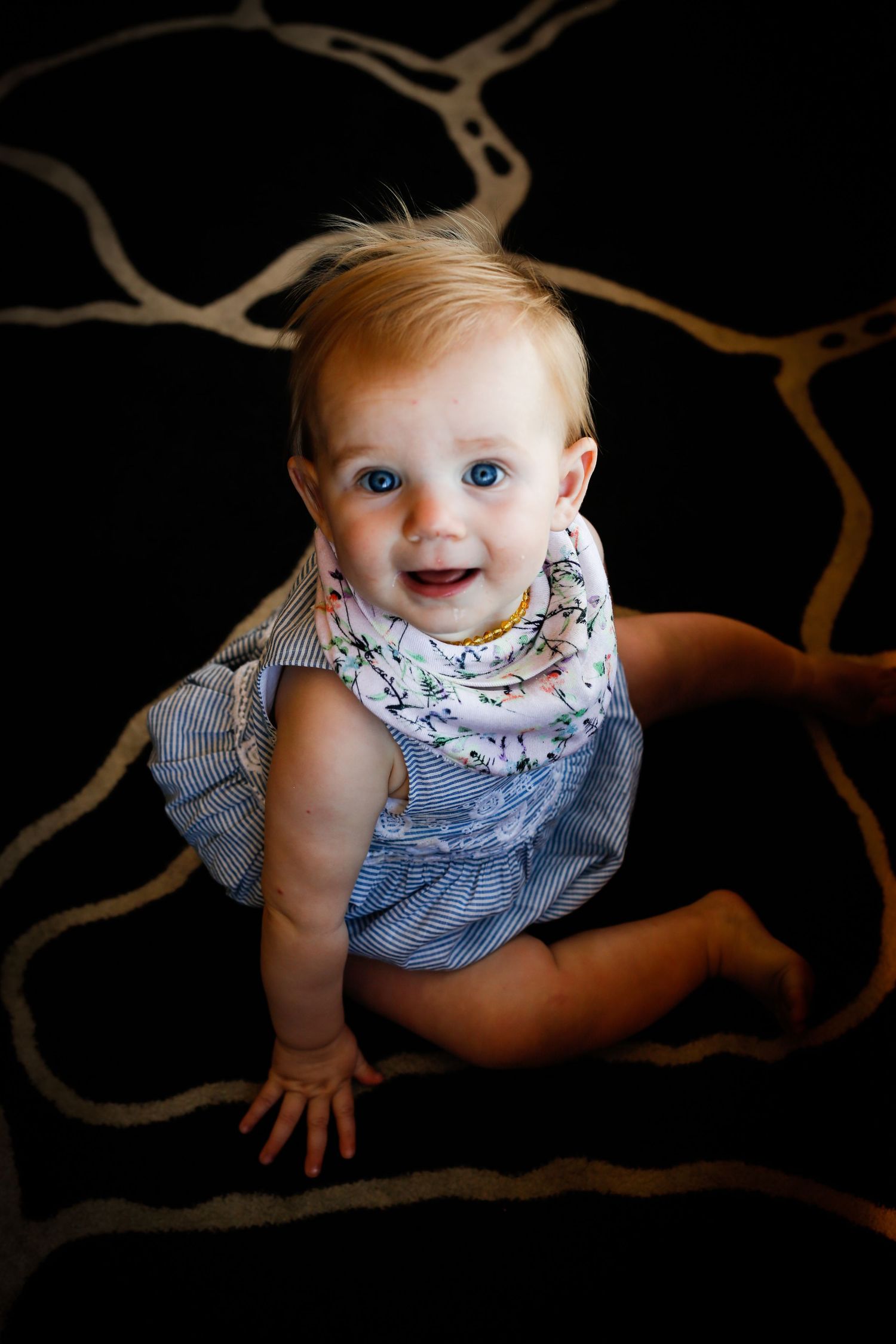 Baby in blue and white dress photographed from above against dark background with tree branch details.