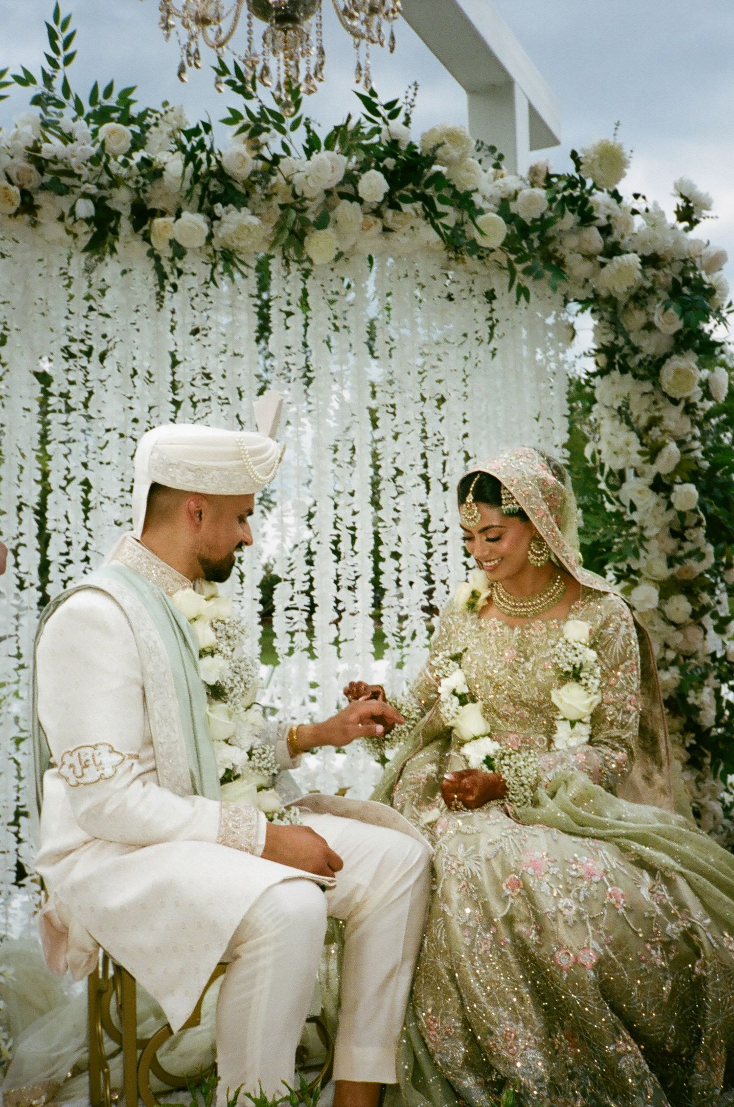 Brown Shia Muslim Desi couple exchange rings under a floral-filled pavilion with a chandelier At revelry675 venue batavia