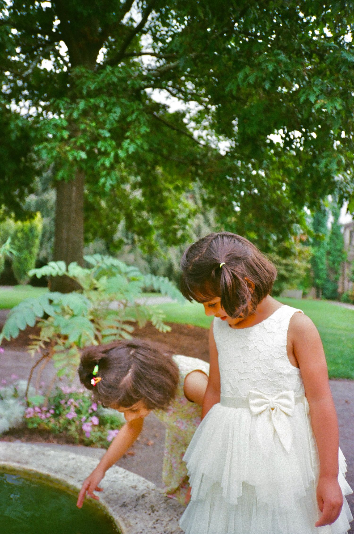 Two girls in white and green play joyfully in a garden, evoking an Italian summer vibe—captured beautifully on 35mm film in Chicago suburbs.