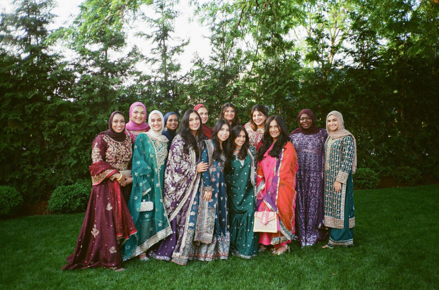 A vibrant group of brown Muslim bridesmaids pose on the grass, wearing colorful outfits full of joy and celebration. the canvas venue