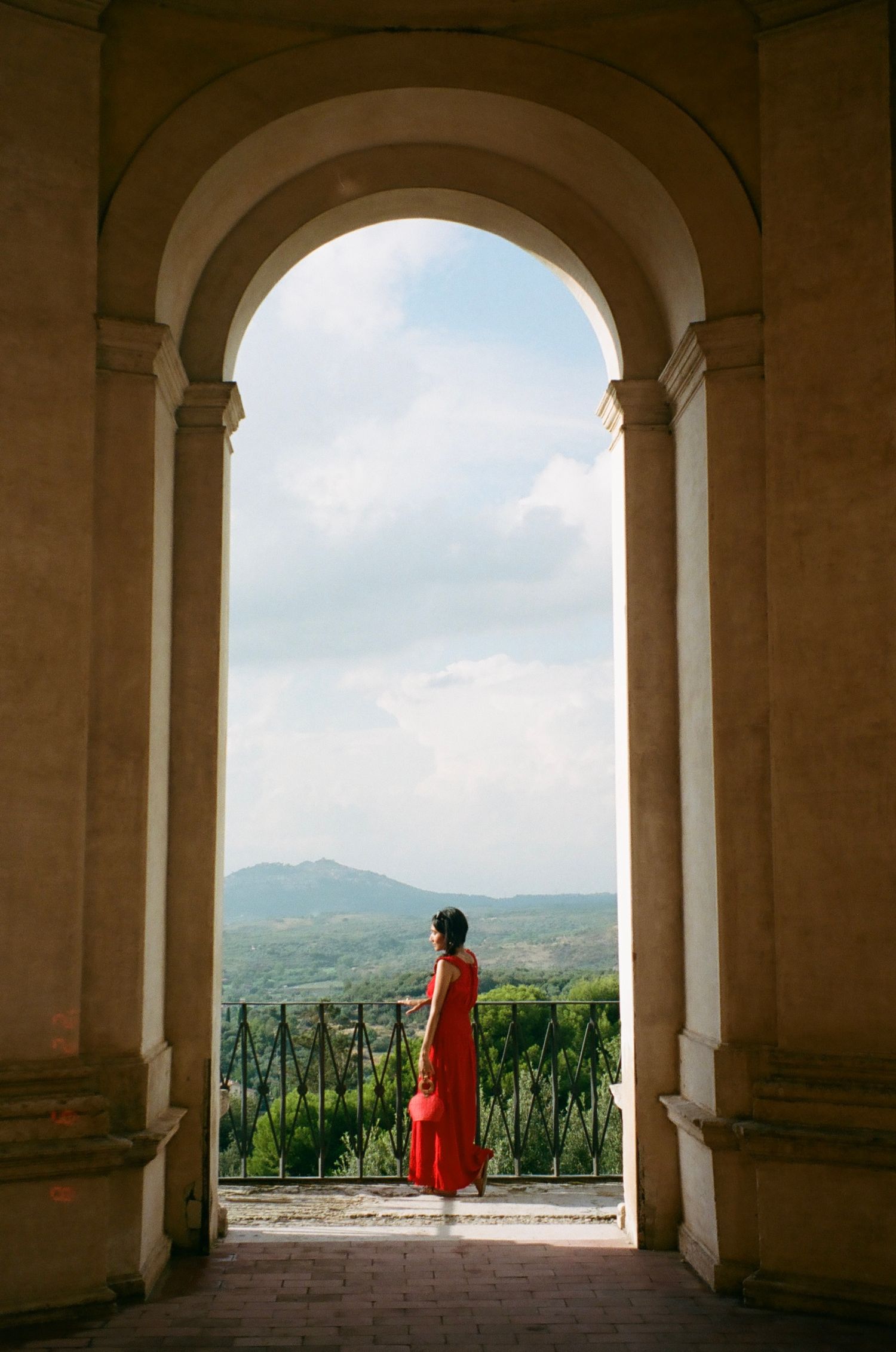 A girl stands gracefully beneath an ancient arch in Italy, captured on 35mm film with beautiful, cinematic light and timeless elegance.