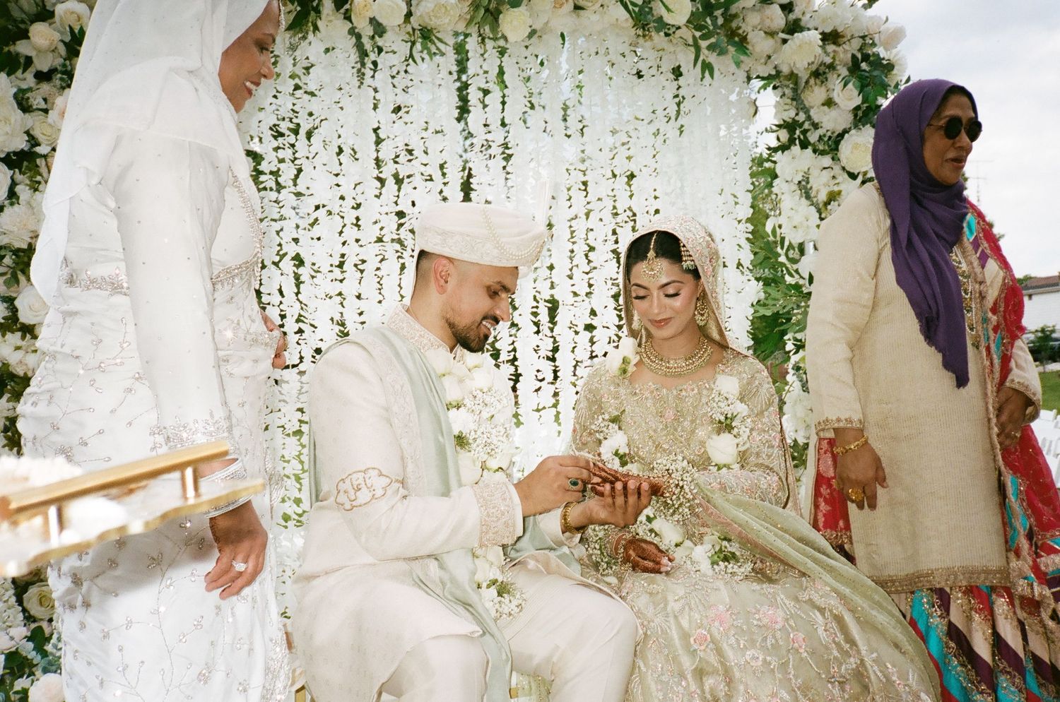 Brown Muslim Desi couple exchange rings under a floral-filled pavilion with a chandelier Shia garden  wedding traditions revelry675 venue