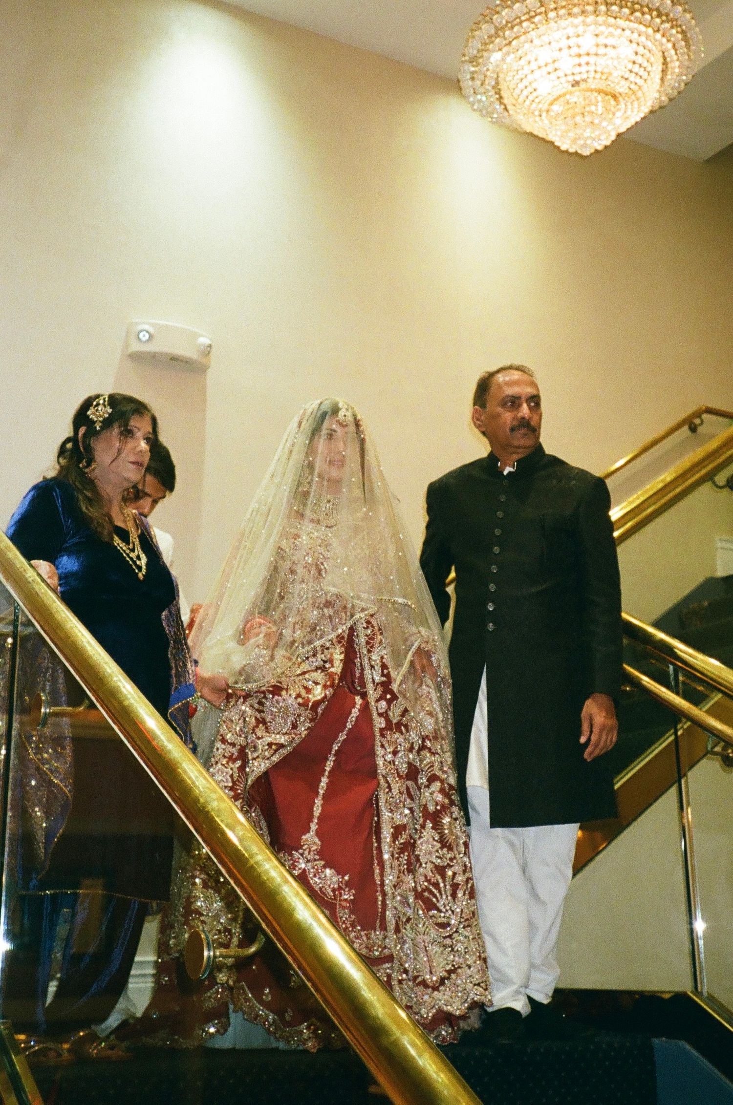Desi Muslim parents walk their daughter down the stairs to her indoor Nikkah ceremony—captured warmly on classic 35mm film. ashyana banquet