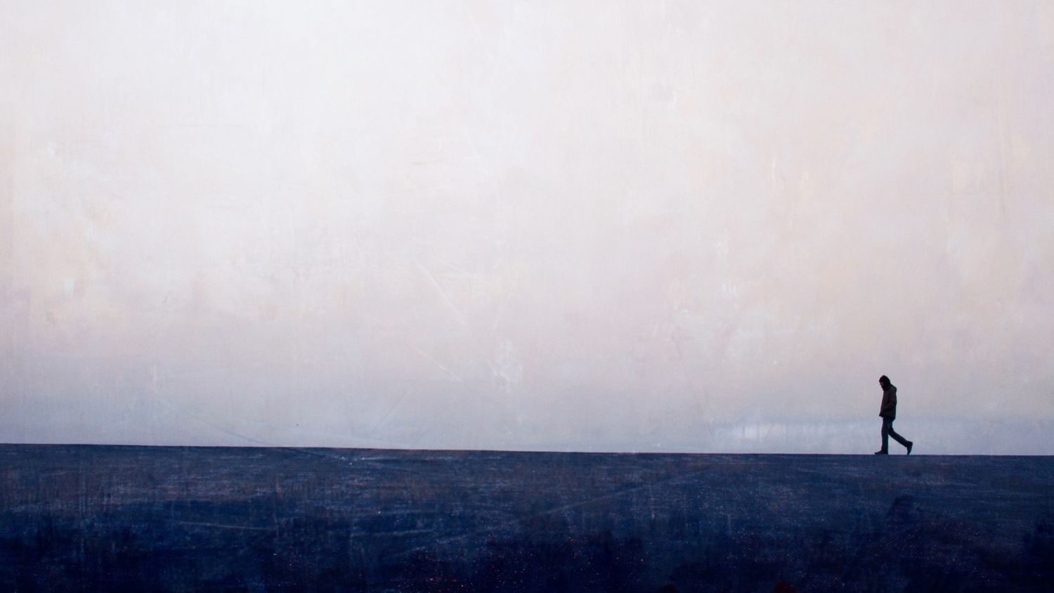 A silhouetted person walking along a misty horizon line at dusk.