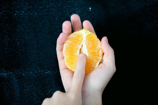 Hands holding and peeling a fresh orange against a dark background.