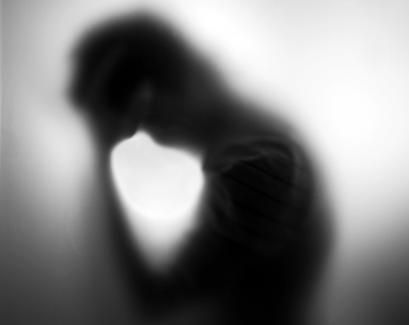 A blurry black and white silhouette behind frosted glass shows a shadowy figure in a contemplative pose.