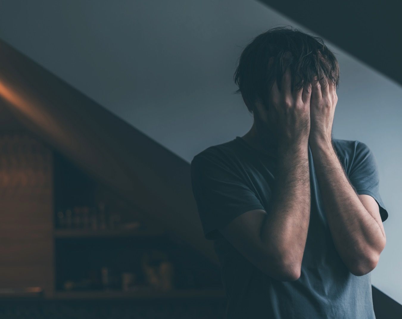 Person covering face with both hands in dark moody setting with dramatic lighting and shadows.