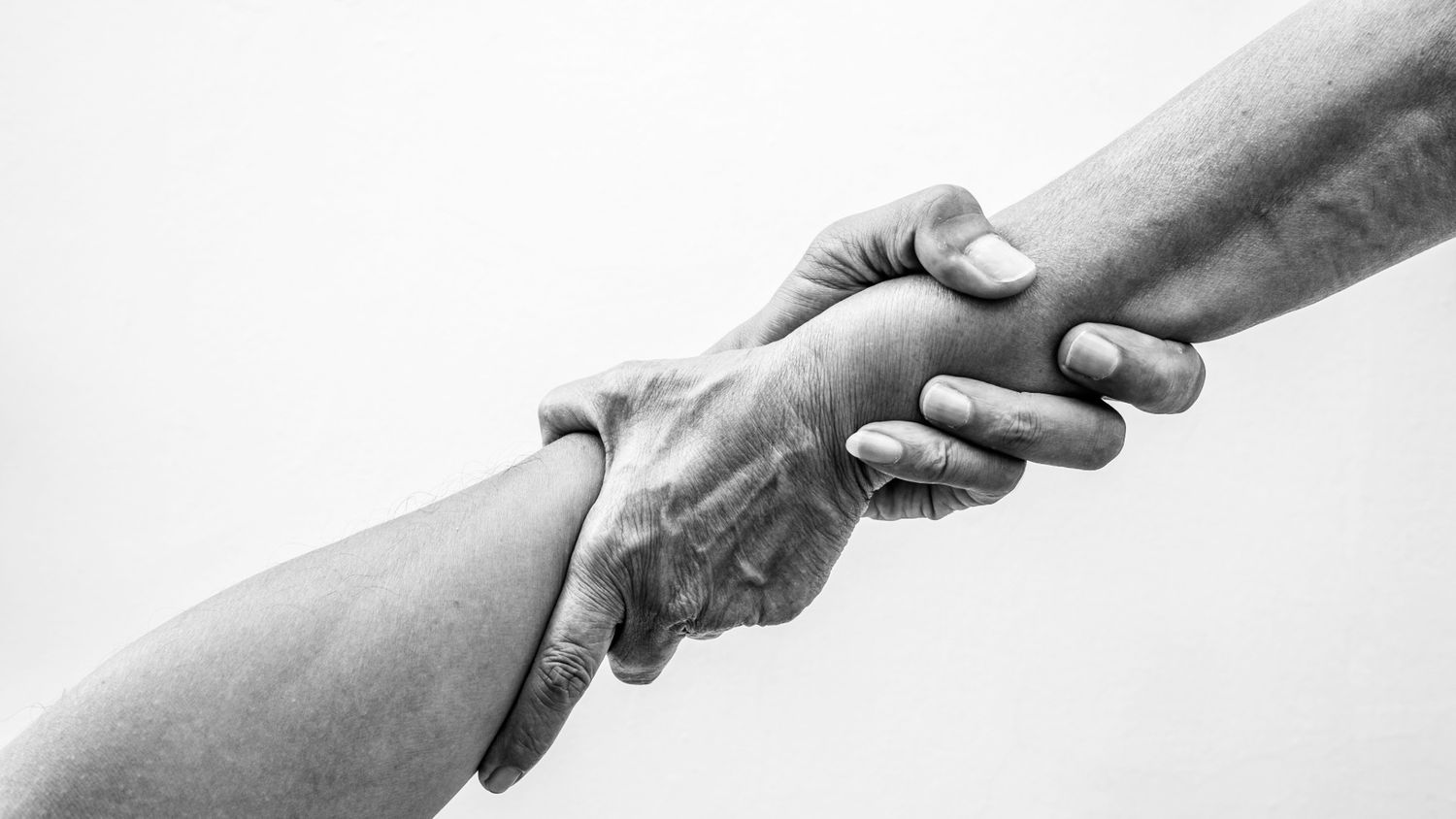 Two hands reaching out to grasp each other in black and white.